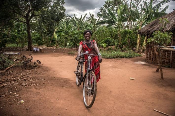 Christine, a VODA community volunteer, with the bike she uses to visit clients, outside her house near Kasawo, Uganda.