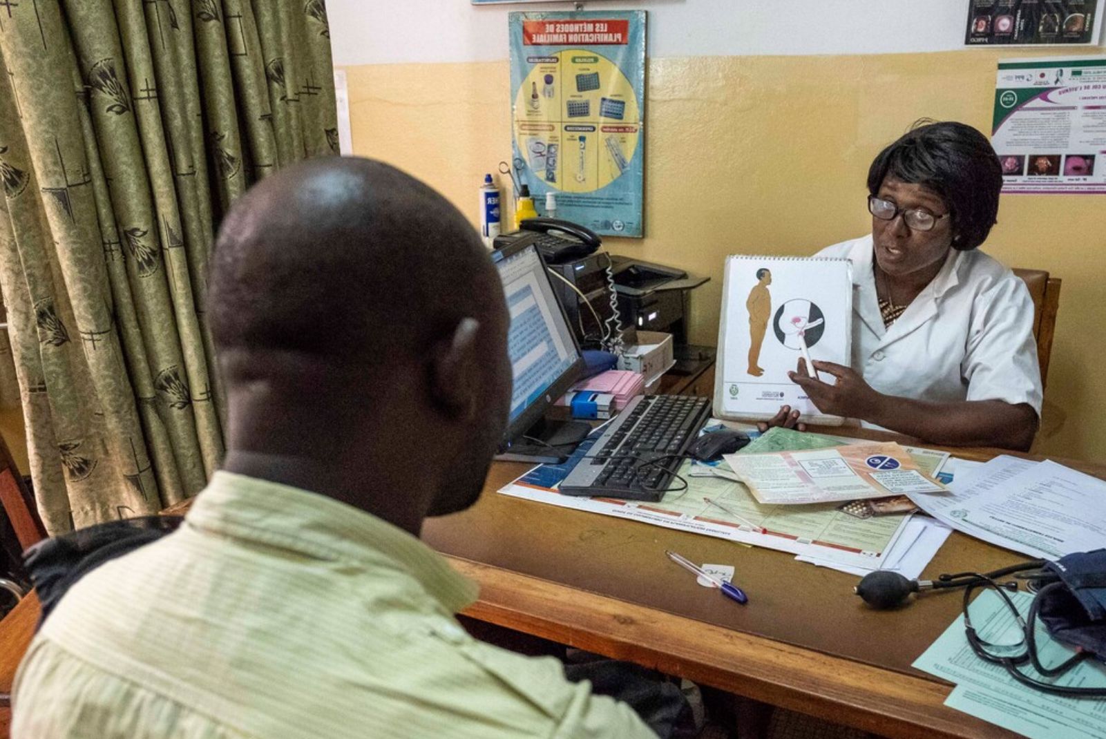 A healthcare worker demonstrates to a patient how a vasectomy works on a poster 