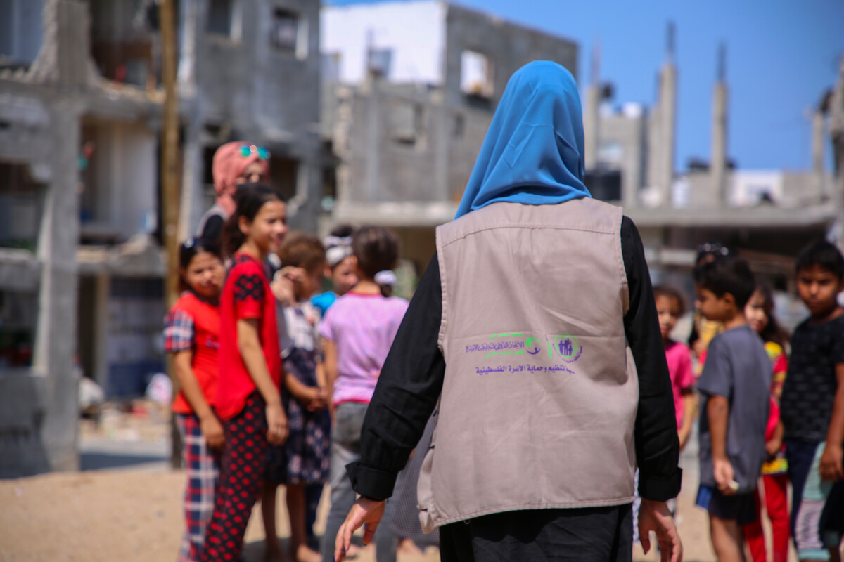 A street view of a female IPPF representative walking towards a group of children gathered together.