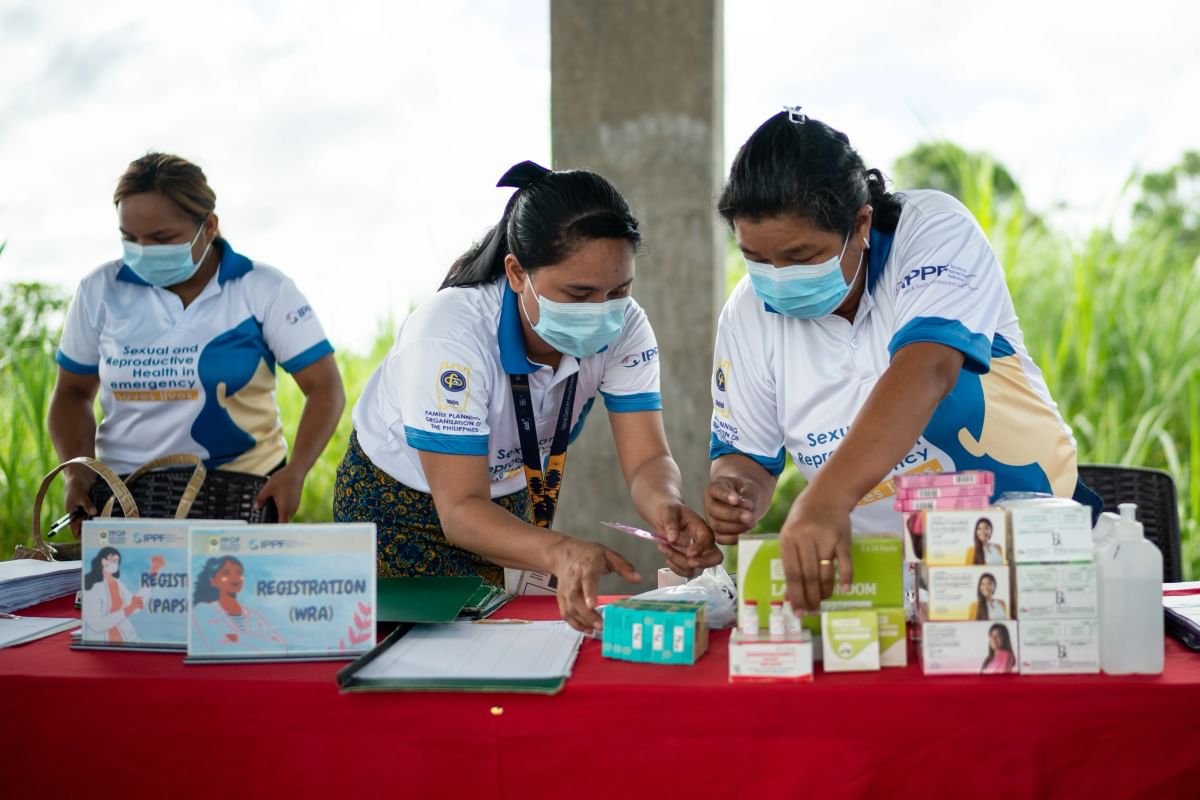 Three FPOP staff stand in behind a table of medical supplies and contraceptives