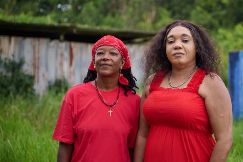 Two community workers in Suriname face the face camera, both dressed in red.