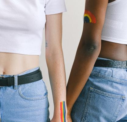 Two women holding hands, one with a Pride flag painted on