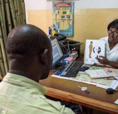 A healthcare worker demonstrates to a patient how a vasectomy works on a poster 