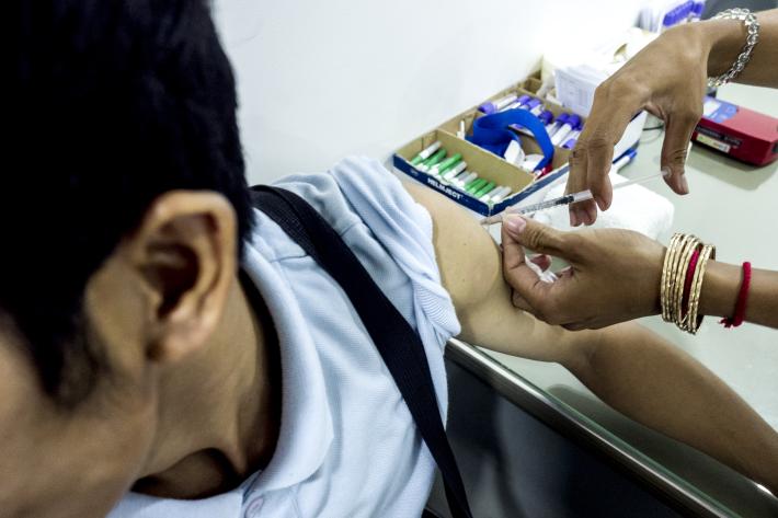 A man, who you cannot see his face is receiving a vaccination by a healthcare professional wearing medical gloves.