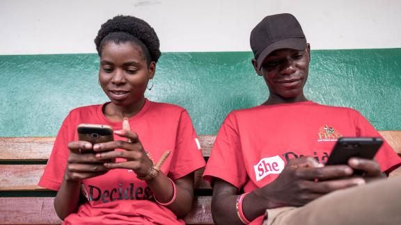 The image shows two people in red t-shirts both holding a mobile phone.