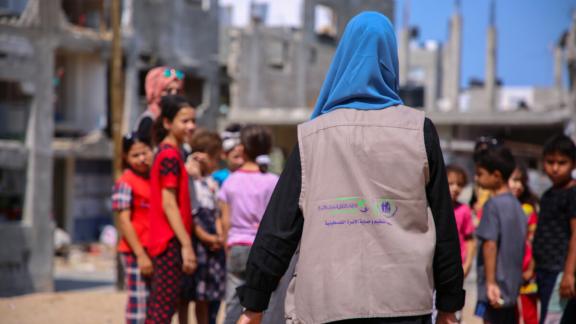 A street view of a female IPPF representative walking towards a group of children gathered together.