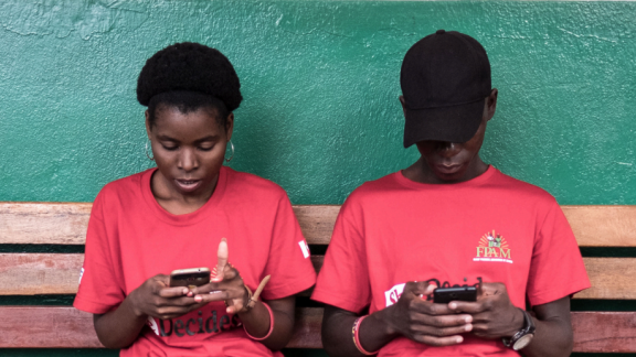 two young people sitting on a bench using their phones