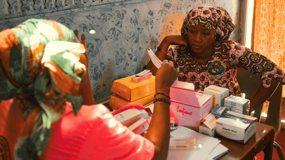 Two women sit at a table with boxes of contraceptives
