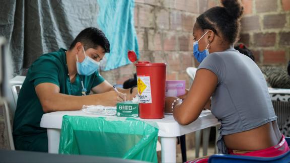A woman speaks with a male healthcare worker, both are wearing face masks.