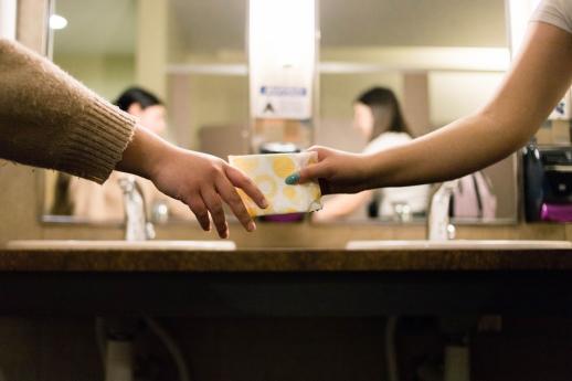 A student hands a sanitary pad to a peer - photo by Annika Gordon, Unsplash